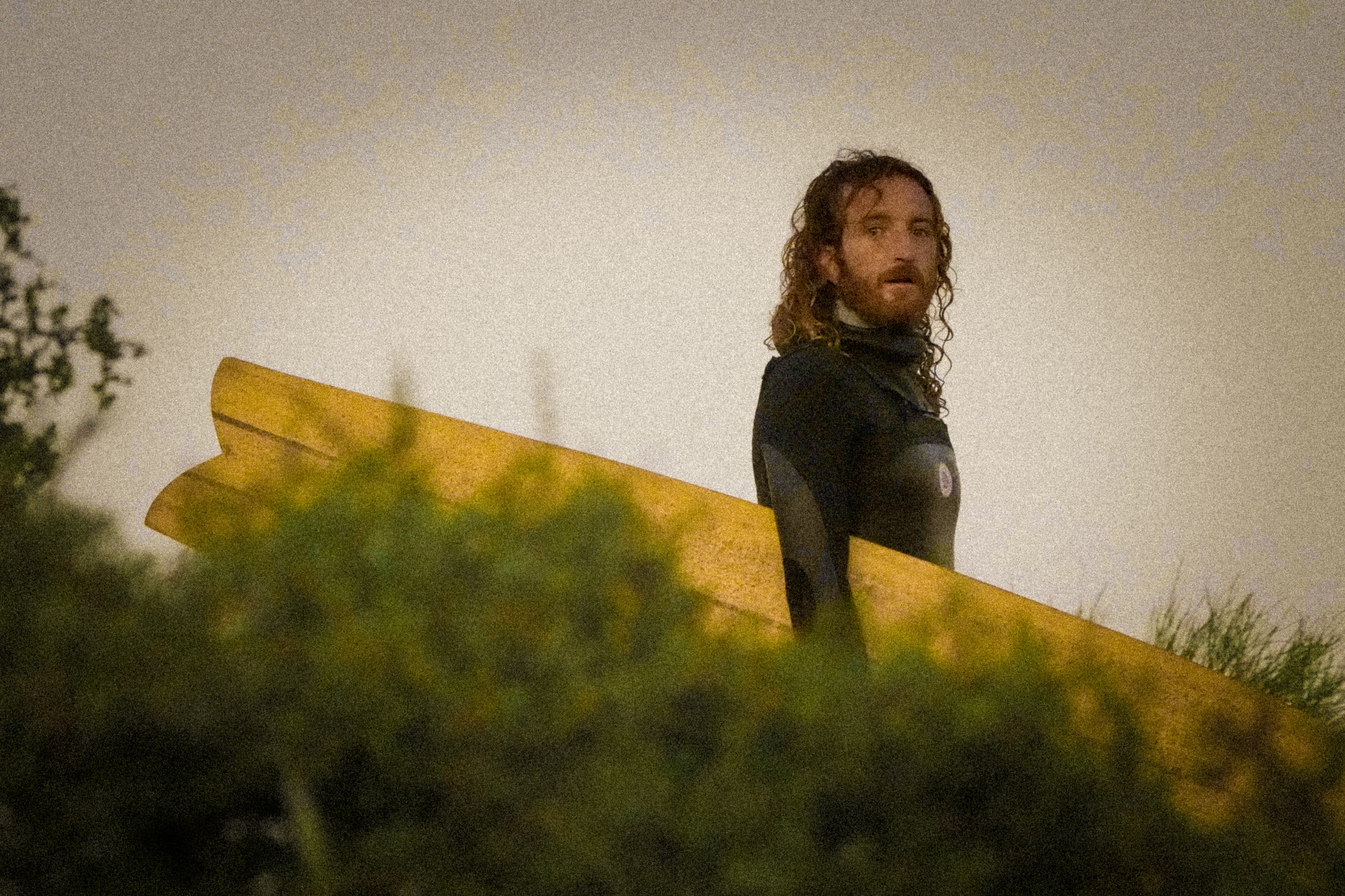 Victor carrying a longboard up from the water at dusk