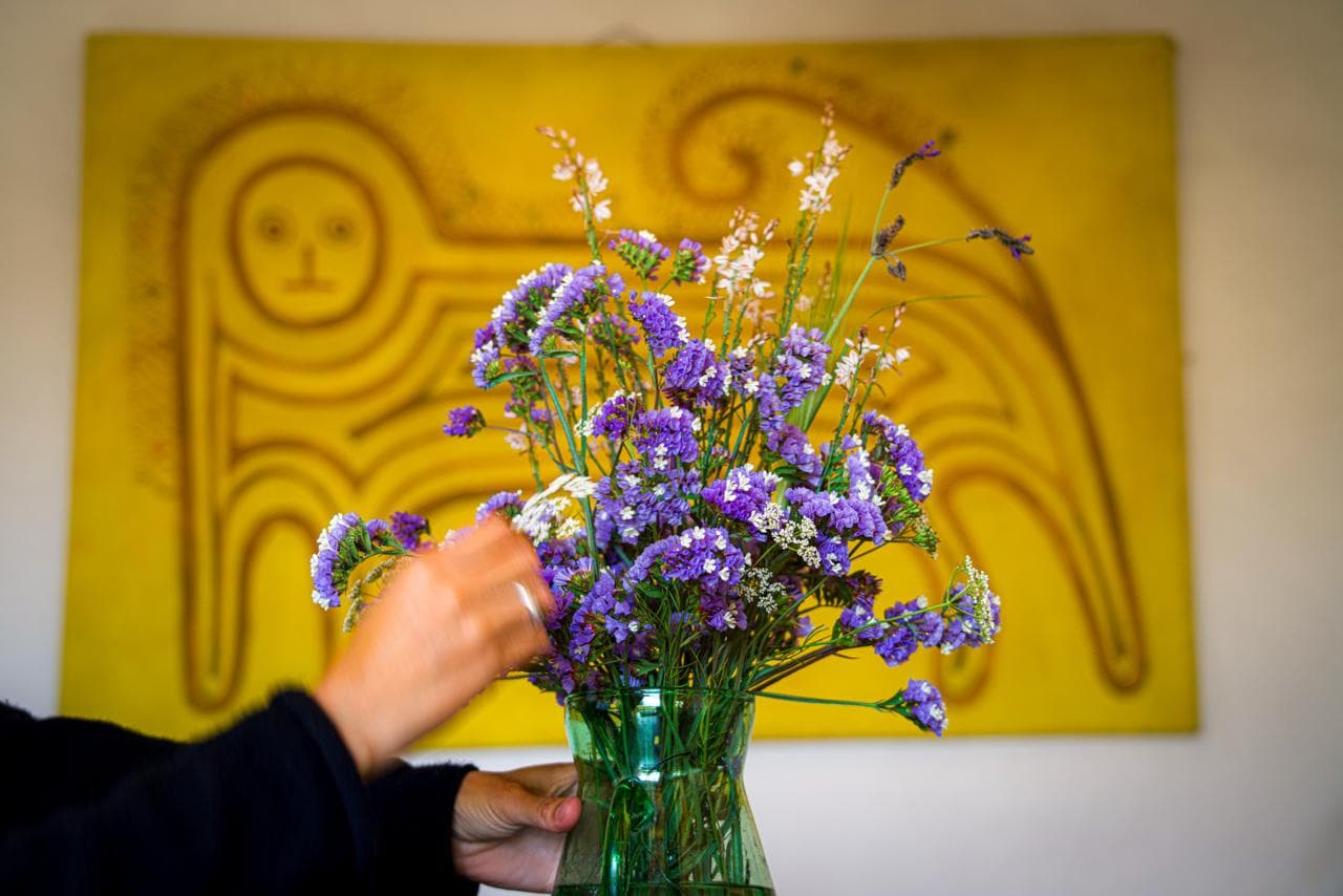 Hands arranging a vase of wildflowers in front of a painting at the house